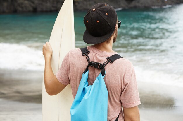 海岸にサーフボードが立っていると彼の前に青い海を見て若い観光客