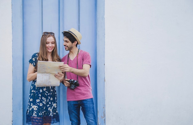 Young tourists with map in front of white wall