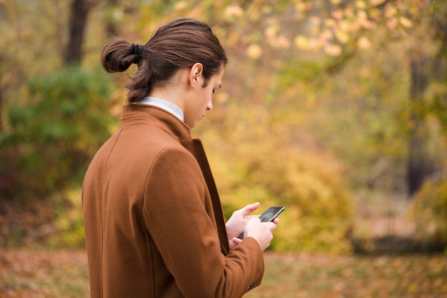 若い旅行者が公園で彼の携帯電話をチェック