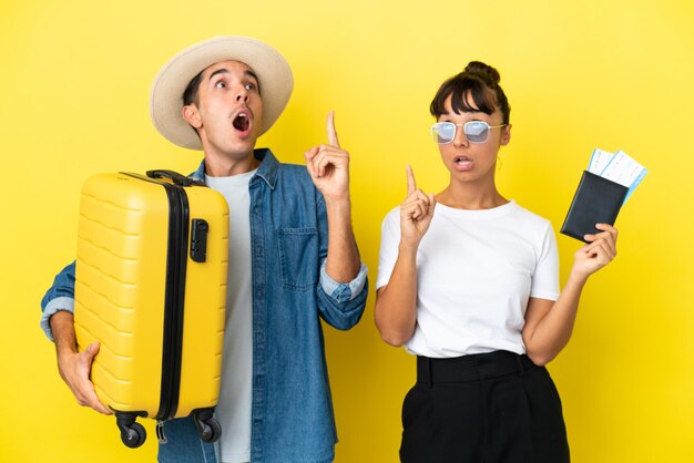 Друзья молодых путешественников держат чемодан и паспорт, изолированные на желтом фоне, думая об идее, указывая пальцем вверх