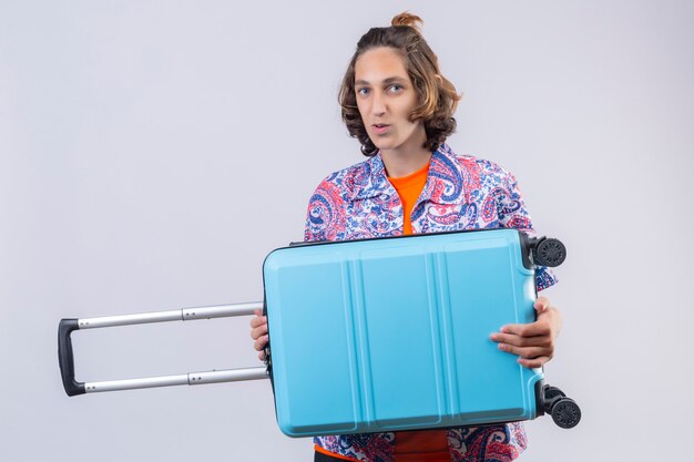 Young traveler man with blue suitcase looking confident smiling with happy face ready to travel standing 