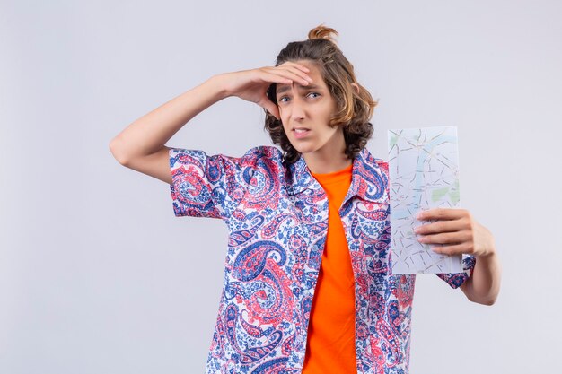 Young traveler man with map looking far away with hand to look something standing over white background