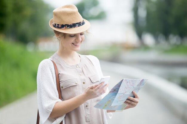 海外旅行中に地図と電話を持っている若い旅行者の女性