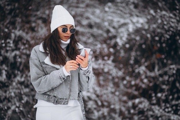 Молодая модная девушка в зимнем парке с помощью телефона
