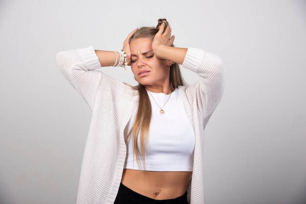 Young troubled woman in white outfit standing on gray background.