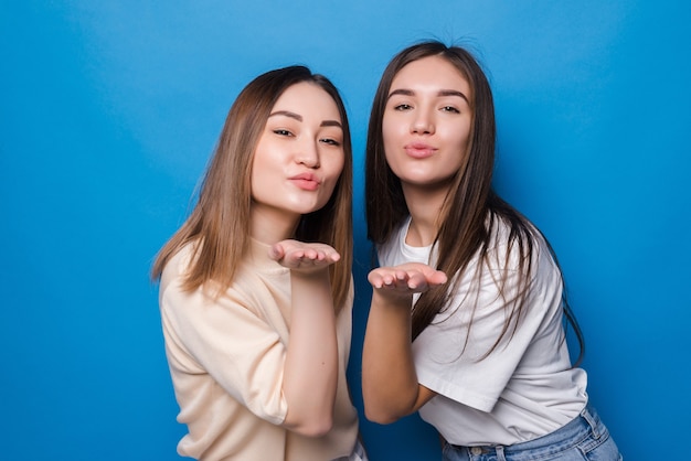 Молодые две женщины воздушный поцелуй изолировали синюю стену