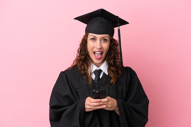 Молодая выпускница университета, изолированная на розовом фоне, удивлена и отправляет сообщение Premium Фотографии