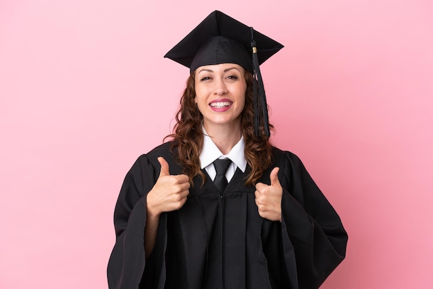 Молодая выпускница университета изолирована на розовом фоне с поднятым вверх пальцем и улыбается