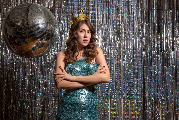 Young upset unhappy charming lady wearing blue green shiny dress with sequins with crown in the party