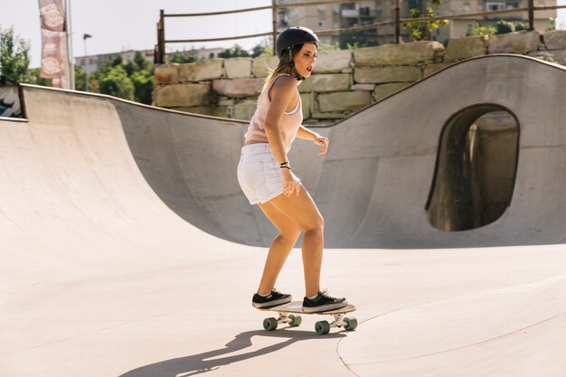 Young urban girl with helmet skating in half pipe