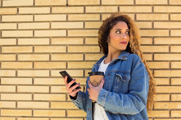 Young urban woman with smartphone in front of brick wall