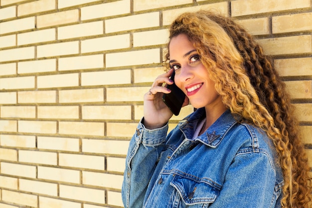 Young urban woman with smartphone in front of brick wall