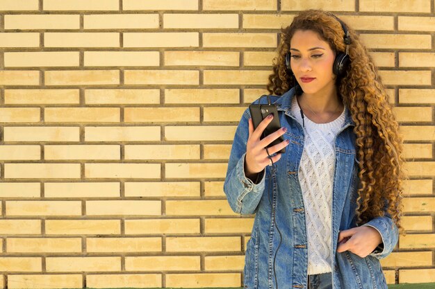 Young urban woman with smartphone in front of brick wall