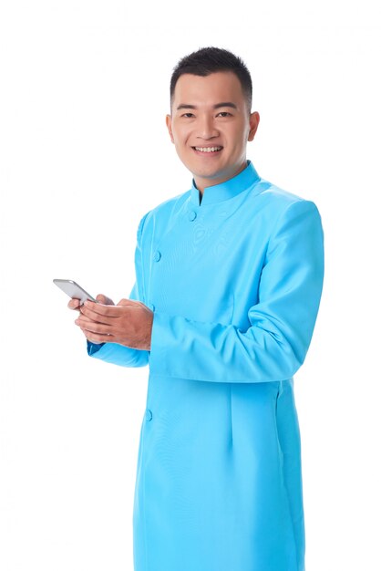 Young Vietnamese man in traditional attire posing in studio and using smartphone