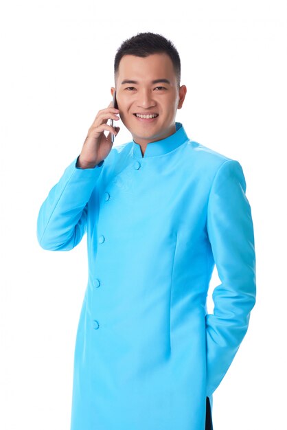 Молодой вьетнамский мужчина в традиционном длинном бирюзовом пиджаке разговаривает по мобильному телефону