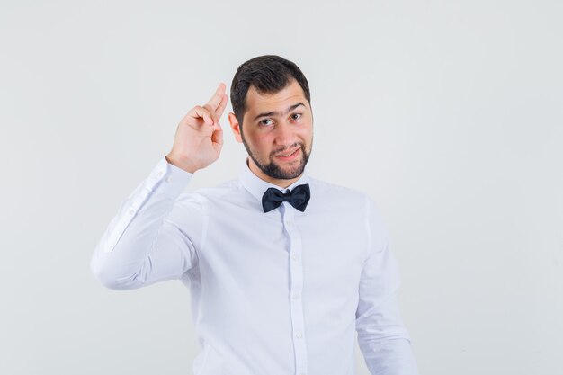 Young waiter gesturing with two fingers in white shirt and looking cheerful. front view.