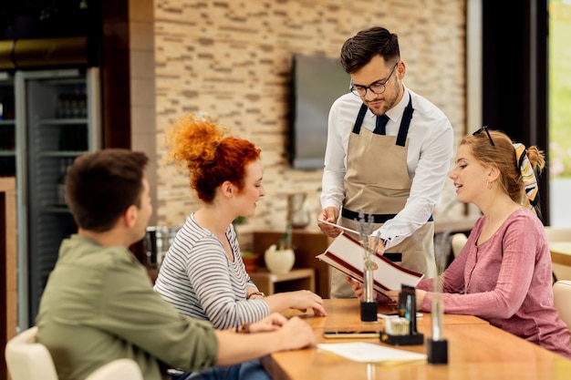 Young waiter recommending to guests what to order from the menu in a cafe