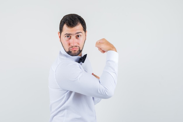 Young waiter showing muscles of arm in white shirt and looking powerful. .