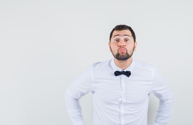 Young waiter in white shirt pouting lips and looking beloved , front view.