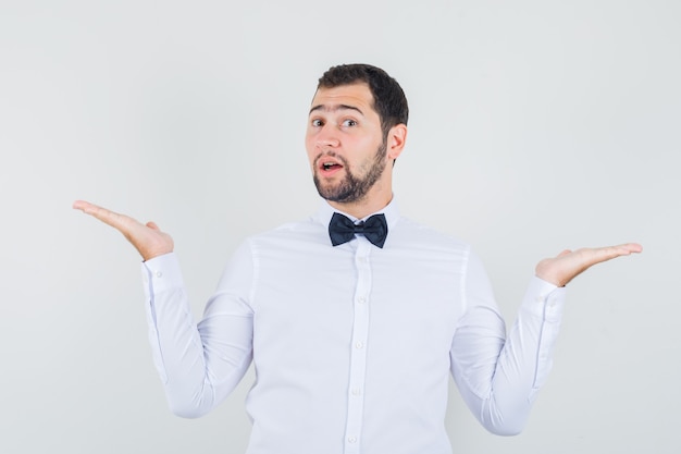 Young waiter in white shirt showing different kinds of meals and drinks and looking cheery , front view.