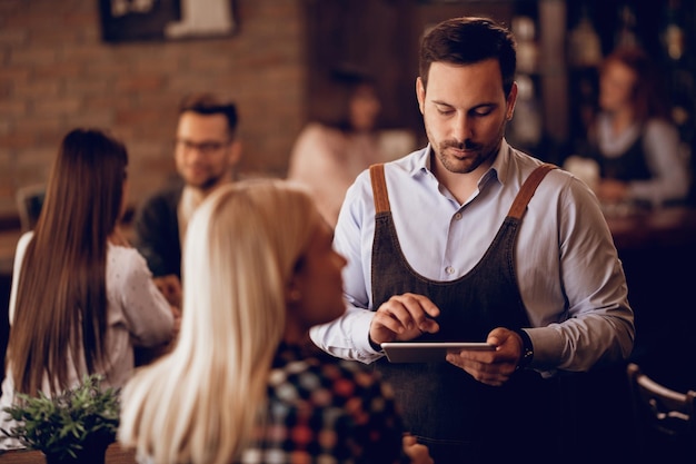 Young waiter writing order on a digital tablet while working in a pub