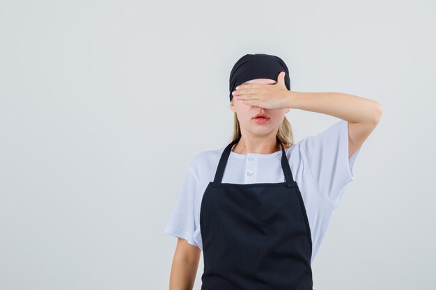 Young waitress covering eyes with hand in uniform and apron