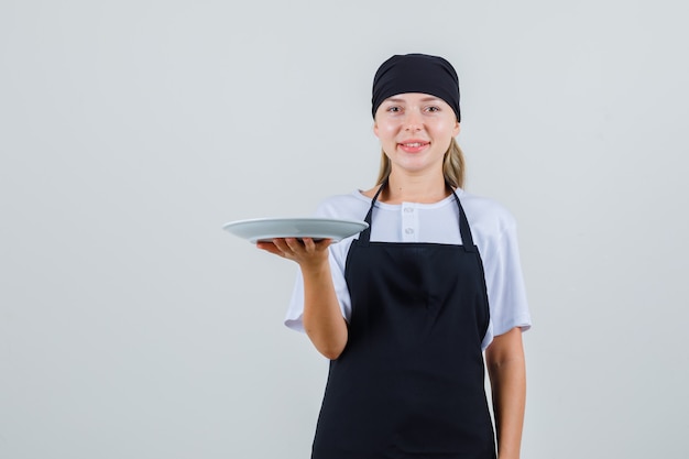 Free photo young waitress holding empty plate in uniform and apron and looking cheerful