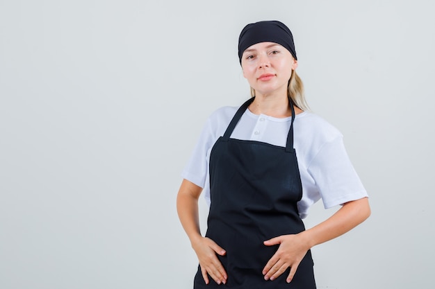 Foto gratuita giovane cameriera che tiene le mani sul suo grembiule in uniforme e sembra ottimista