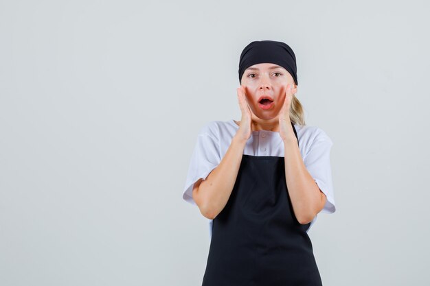 Young waitress holding hands near mouth in uniform and apron