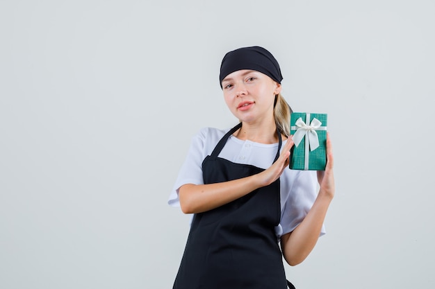 Young waitress holding present box in uniform and apron and looking positive