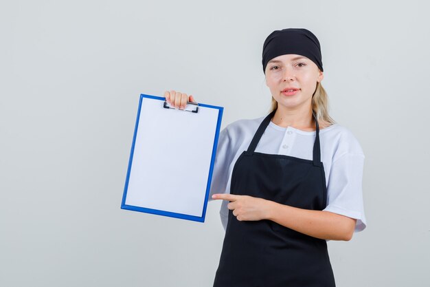 Young waitress pointing at clipboard in uniform and apron