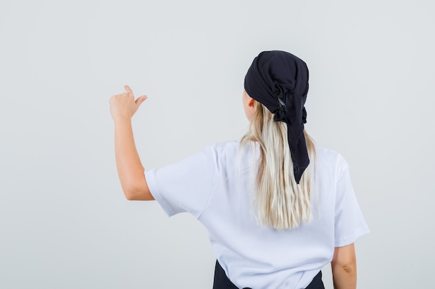 Young waitress pointing at something in uniform and apron back view.