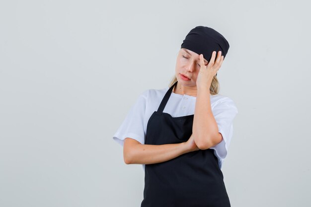 Young waitress propping head on raised hand in uniform and apron and looking tired