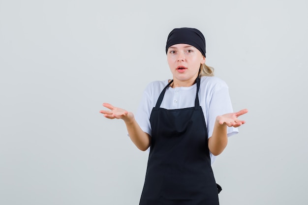 Young waitress raising hands like holding tray in uniform and apron