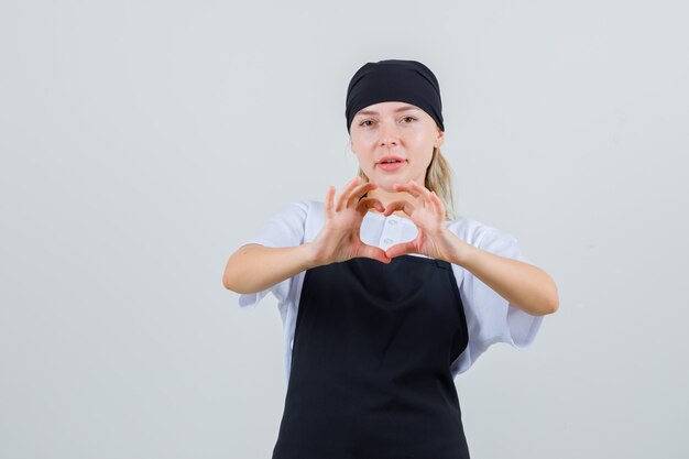Молодая официантка показывает жест сердца в форме и фартуке