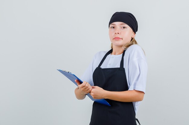 Young waitress in uniform and apron holding clipboard