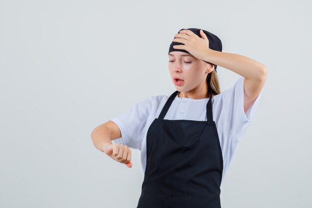 Young waitress in uniform and apron looking at her arm and looking confused