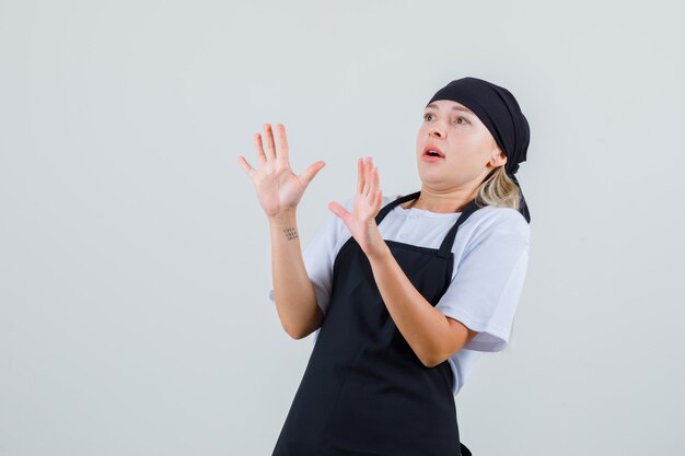 Young waitress in uniform and apron showing refusal gesture and looking scared