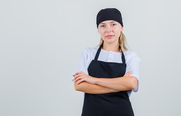 Giovane cameriera in uniforme e grembiule in piedi con le braccia incrociate e guardando fiducioso