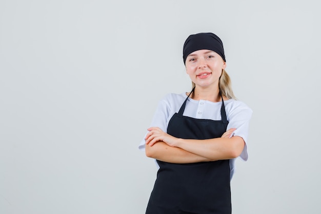 Young waitress in uniform and apron standing with crossed arms and looking glad