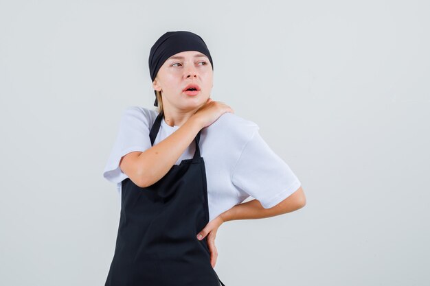 Young waitress in uniform and apron suffering from back pain and looking tired