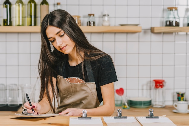 Free photo young waitress writing on clipboard