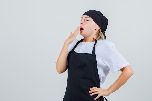 Free photo young waitress yawning in uniform and apron and looking sleepy