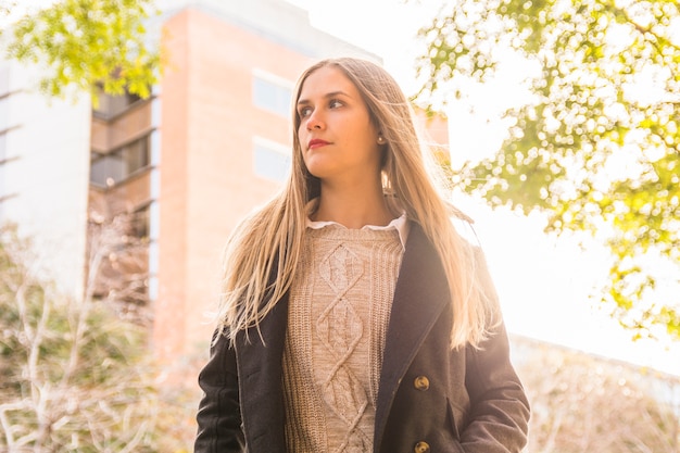 Young warm clothed female model standing in shiny park