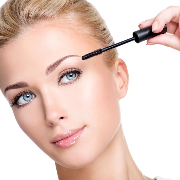 Young white woman applying mascara on eyelashes  - macro shot over white wall