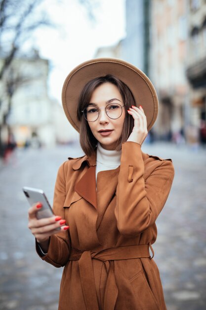 Молодые в широкой шляпе текстовые сообщения на смартфоне осенней улице