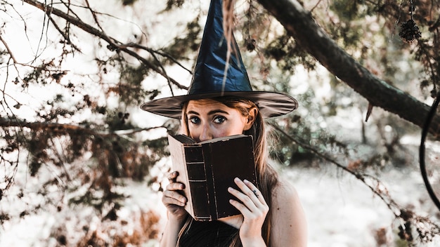 Young witch hiding in old book in sunny forest