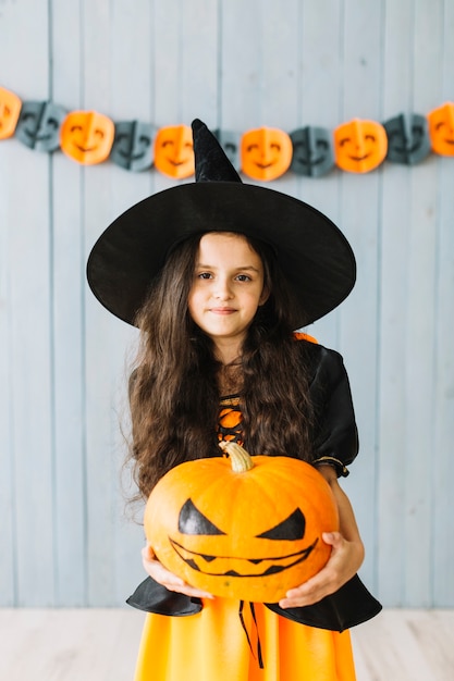 Young witch holding pumpkin at Halloween party