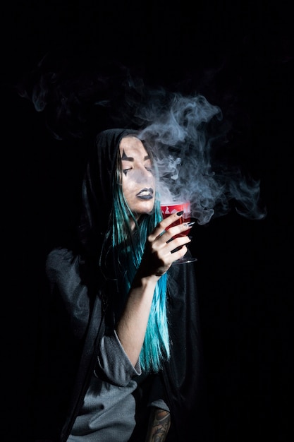 Молодая ведьма в капюшоне с малиновым дымчатым кубком