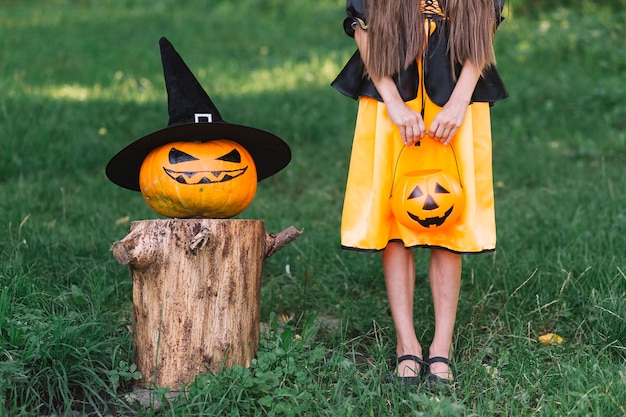 Young witch and jack-o-lantern standing in forest on Halloween
